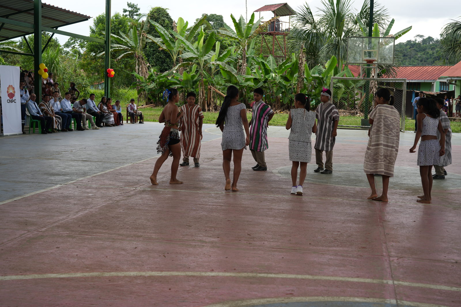 Danza tradicional en la losa deportiva, con la selva y la escuela al fondo.