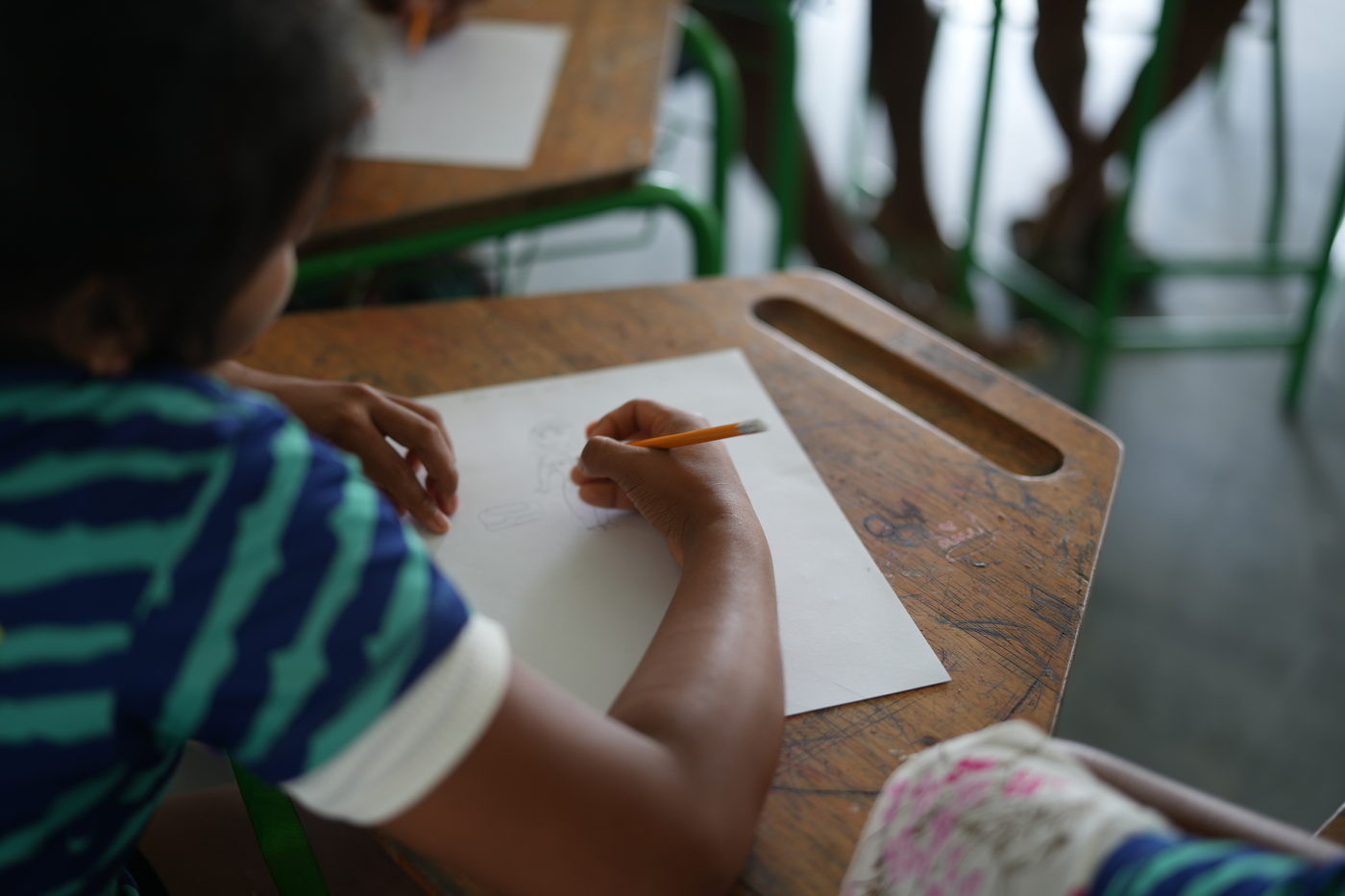 Una hoja en blanco sobre una carpeta de madera en el aula de Ticumpinía, con un lápiz a punto de escribir.